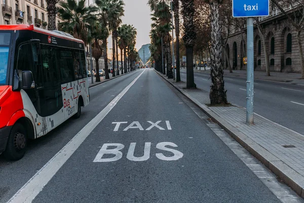 BARCELONA, ESPAÑA - 28 DE DICIEMBRE DE 2018: calle tranquila con edificio y palmeras, y autobús en movimiento por la carretera - foto de stock