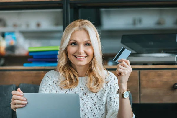 Mujer feliz celebración de la tarjeta de crédito mientras se utiliza el ordenador portátil en casa - foto de stock