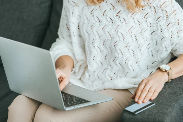 Vista ritagliata della donna che utilizza il computer portatile vicino alla carta di credito a casa — Foto stock