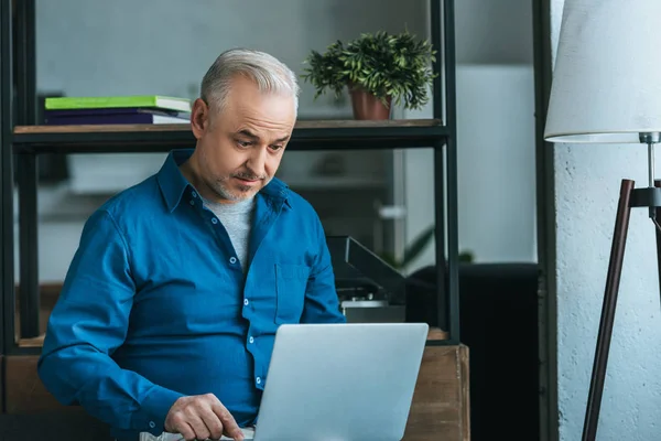 Homem bonito usando laptop enquanto sentado em casa — Fotografia de Stock