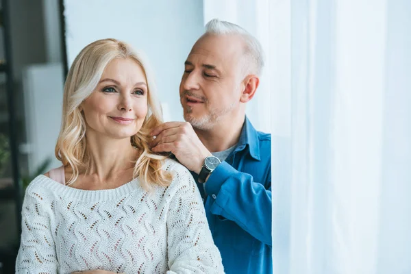 Весёлый мужчина смотрит на светлые волосы улыбающейся жены дома — стоковое фото