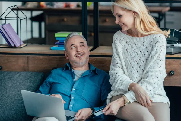 Cheerful man using laptop near attractive wife holding credit card — Stock Photo