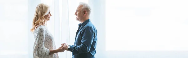 Fröhliches Paar hält Händchen und schaut sich am heimischen Fenster an — Stockfoto