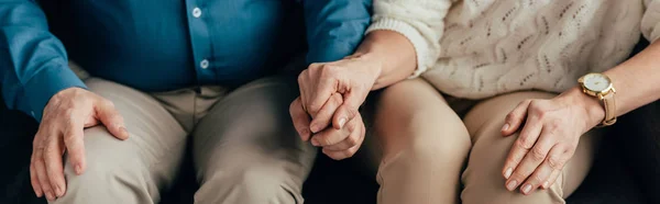 Vista recortada de la pareja cogida de la mano mientras está sentada en casa — Stock Photo