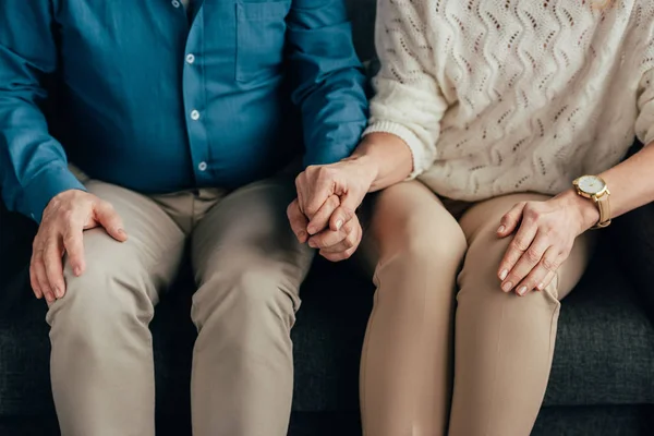 Vista recortada del hombre y la mujer tomados de la mano mientras están sentados en casa - foto de stock