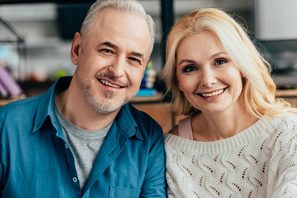 Feliz marido y mujer mirando a la cámara y sonriendo en casa - foto de stock