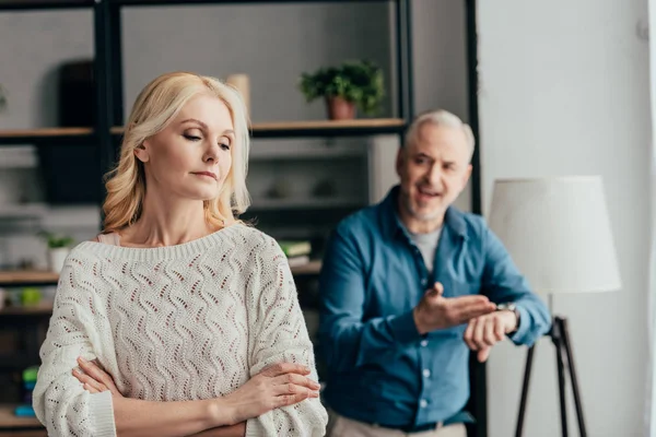 Selective focus of woman standing with crossed arms while husband arguing on background — Stock Photo