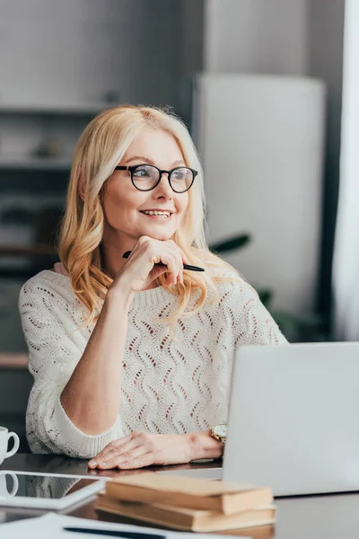 Selective focus of cheerful woman in glasses sitting near laptop — Stock Photo