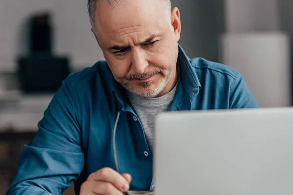 Foco seletivo de homem cansado bonito olhando para laptop em casa — Fotografia de Stock