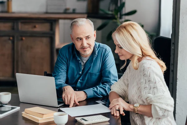 Handsome man pointing with finger at blank paper while looking at attractive blonde wife — Stock Photo