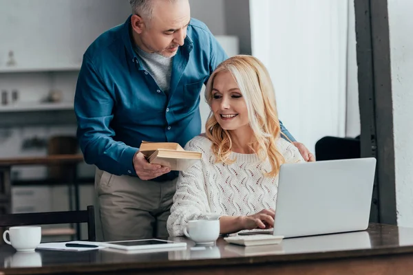 Schöner Mann hält Bücher neben fröhlicher Frau mit Laptop — Stockfoto