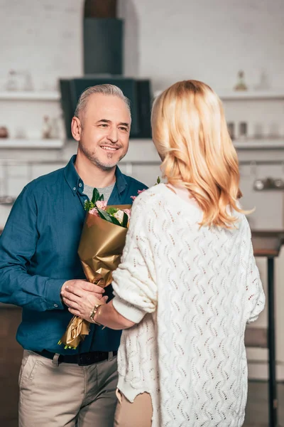 Fröhlicher Mann lächelt, während er der blonden Frau Blumen schenkt — Stockfoto