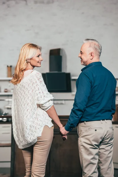 Feliz pareja de pie y sonriendo mientras toma de la mano - foto de stock