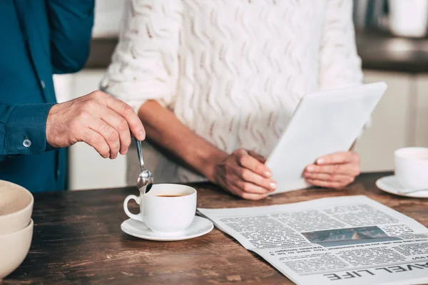 Vue recadrée de l'homme tenant cuillère près de tasse avec café près de la femme tenant tablette numérique — Photo de stock