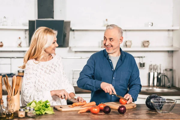 Coppia allegra taglio carota e pomodoro e sorridente in cucina — Foto stock