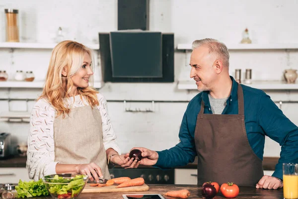 Schöner Mann gibt lächelnde Frau in Küche rote Zwiebel — Stockfoto