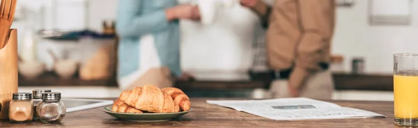 Foco seletivo de croissants na chapa perto de vidro de suco de laranja com par no fundo — Fotografia de Stock