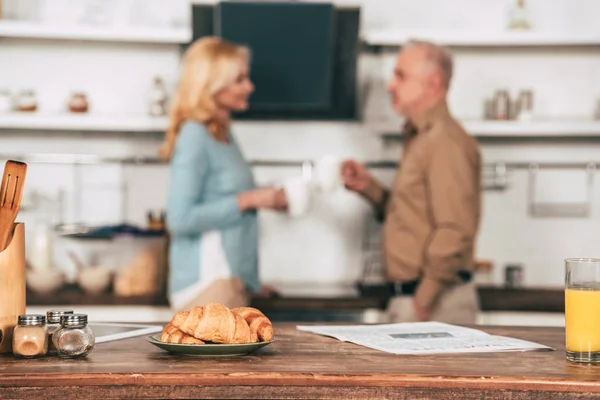 Selective focus of tasty croissants on plate near glass of orange juice with couple on background — Stock Photo