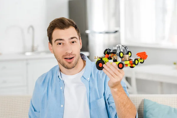 Eccitato bell'uomo guardando la macchina fotografica e tenendo auto giocattolo a casa — Foto stock