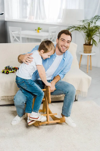 Happy father and preschooler son playing with wooden rocking horse at home — Stock Photo