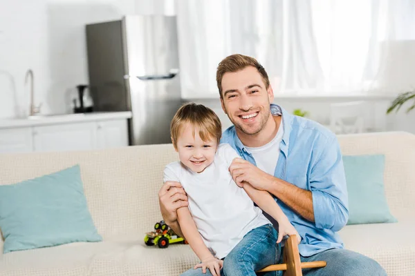 Glücklicher Vater umarmt Sohn und schaut zu Hause in die Kamera — Stockfoto