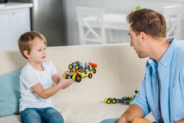 Adorable preescolar hijo mostrando juguete coche a padre en casa - foto de stock