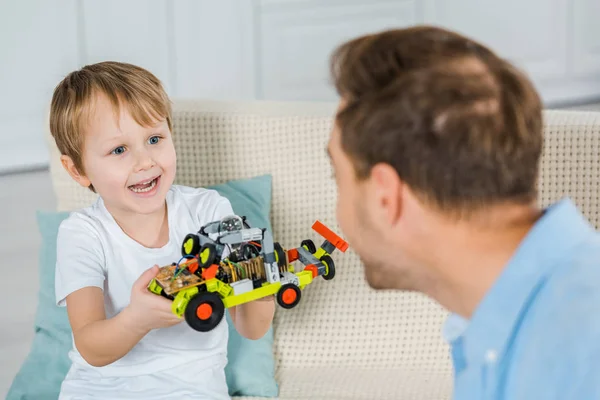 Adorable smiling preschooler son showing toy car to father at home — Stock Photo