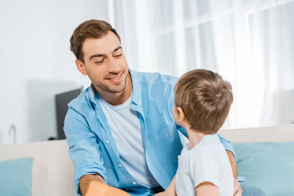 Feliz padre guapo mirando hijo preescolar en casa - foto de stock