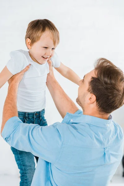 Padre sosteniendo feliz hijo preescolar en las manos en casa - foto de stock