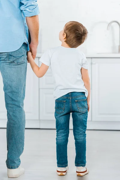 Vista posteriore del bambino in età prescolare che si tiene per mano con il padre a casa — Foto stock