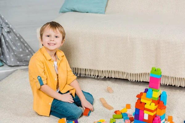 Очаровательный дошкольник, играющий с красочными строительными блоками дома — стоковое фото