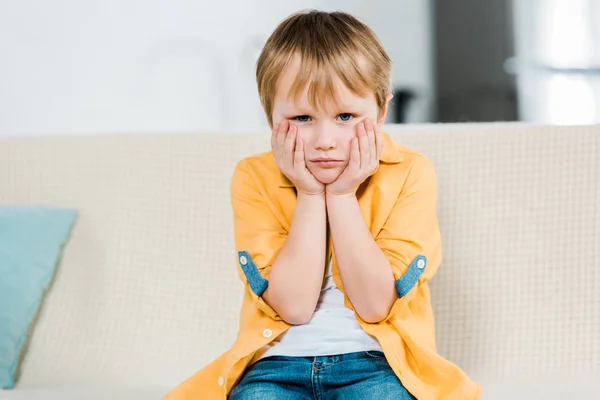 Unzufriedener Vorschulkind sitzt, stützt Gesicht mit Händen ab und schaut zu Hause in die Kamera — Stockfoto