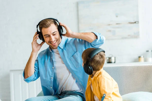 Красивый улыбающийся отец с сыном-дошкольником в наушниках, слушающим музыку дома — стоковое фото