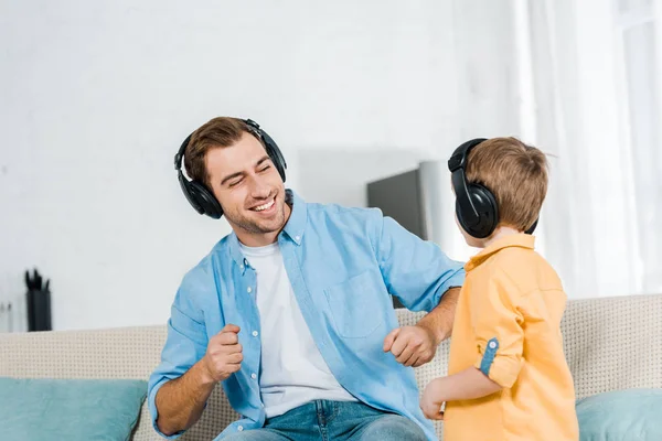 Счастливый отец с дошкольным сыном в наушниках слушает музыку дома — стоковое фото