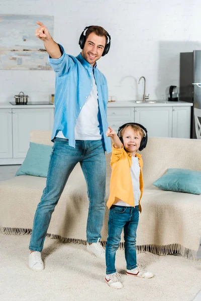 Glücklicher Vater mit Vorschulsohn im Kopfhörer, der zu Hause Musik hört und mit den Fingern zeigt — Stockfoto
