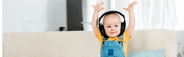 Adorable mâle tout-petit dans les écouteurs avec les mains dans l'air écouter de la musique à la maison avec espace de copie — Photo de stock