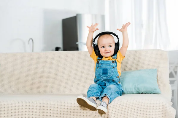 Adorável criança do sexo masculino em fones de ouvido com as mãos no ar ouvir música em casa com espaço de cópia — Fotografia de Stock