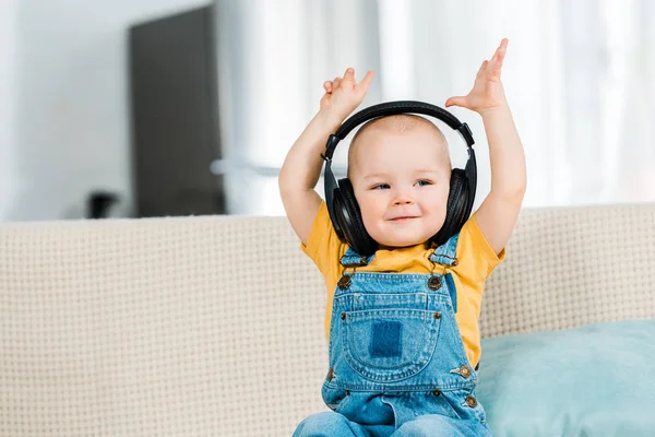 Очаровательный мальчик в наушниках с руками в воздухе слушает музыку дома — стоковое фото