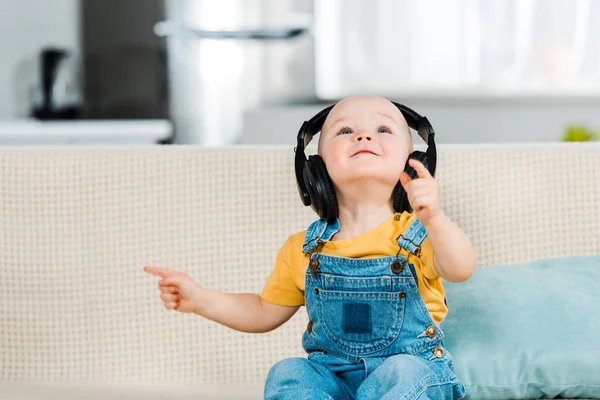 Adorable male toddler in headphones sitting on couch and listening music at home — Stock Photo