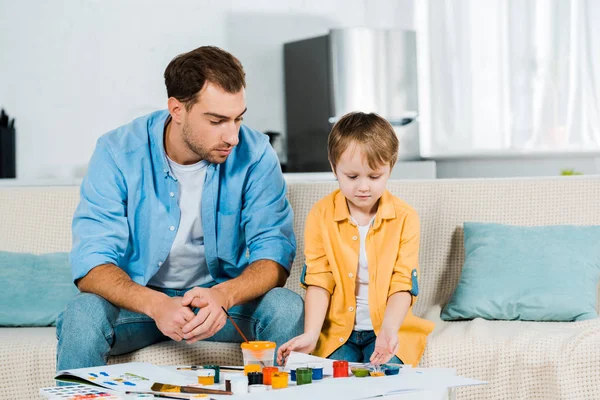 Padre e figlio in età prescolare seduto con forniture artistiche durante il disegno a casa — Foto stock