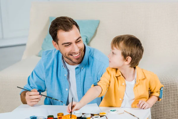 Feliz padre e hijo preescolar sosteniendo pinceles y dibujando en casa - foto de stock