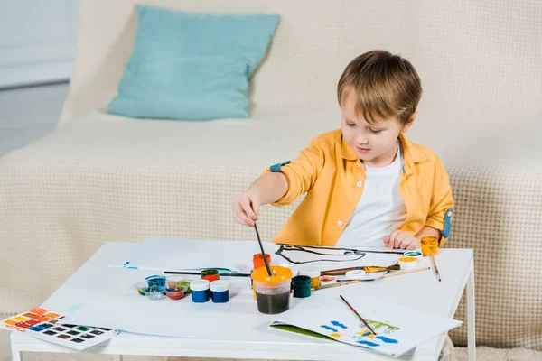 Lindo niño preescolar dibujo con pincel en casa - foto de stock