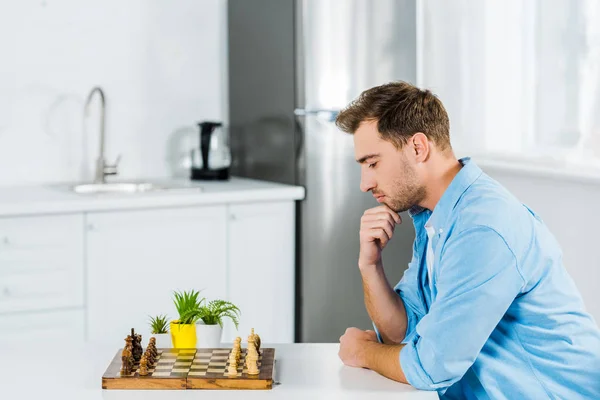 Nachdenklicher Mann sitzt zu Hause am Tisch und spielt Schach — Stockfoto