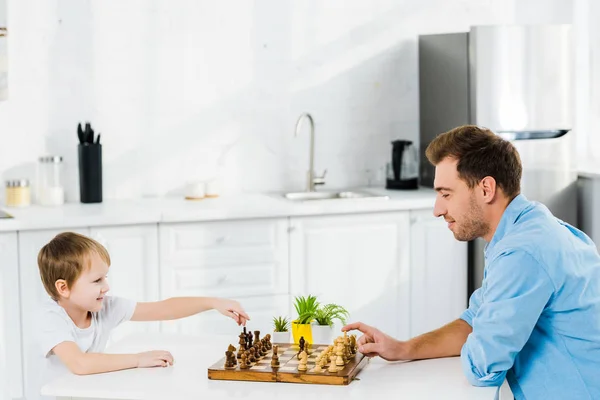 Father and adorable preschooler son playing chess in kitchen with copy space — Stock Photo