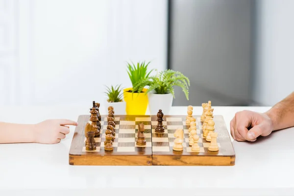 Vista cortada de homem e menino jogando xadrez na mesa com plantas — Fotografia de Stock