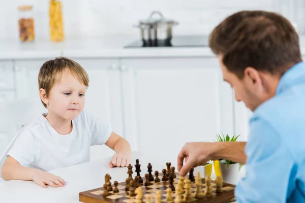 Отец и дошкольник сын сидит за столом и играет в шахматы дома — стоковое фото