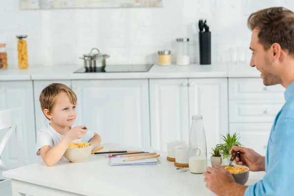 Padre e hijo preescolar comiendo cereales durante el desayuno en la cocina - foto de stock