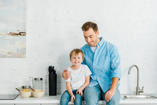 Glücklicher Vater und Vorschulsohn mit Schalen auf Müsli auf der Theke beim Frühstück in der Küche — Stockfoto