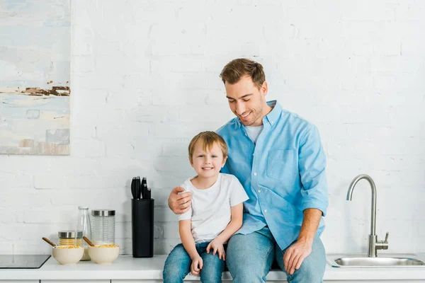 Felice padre e figlio in età prescolare con ciotole su cereali sul bancone durante la colazione in cucina — Foto stock