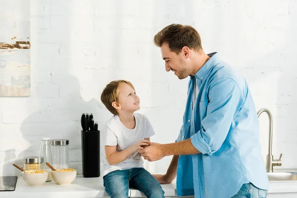 Father and preschooler son with bowls on cereal on counter during breakfast in kitchen — Stock Photo